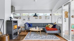 Een gezellige woonkamer met een open haard, een grijze bank, een bijzettafeltje en een kamerkleed met een patroon.