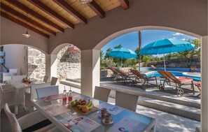 Un'area pranzo all'aperto coperta con piscina e ombrelloni, pareti in pietra e mobili in vimini.