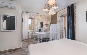 Camera da letto con parete in pietra, una vasca da bagno bianca, un lampadario e un letto grande.