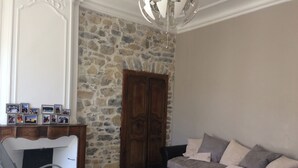 Un salon avec un mur en pierre, une porte en bois, un canapé, un fauteuil à bascule et une petite table.