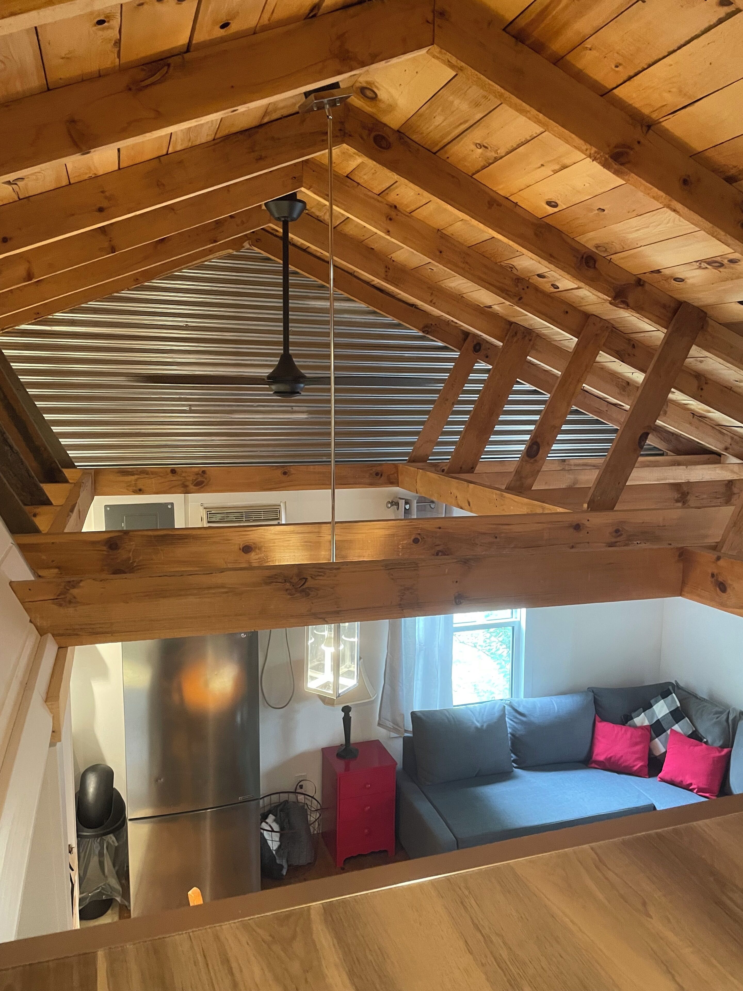Un espacio tipo loft con vigas de madera a la vista, una lámpara colgante, un banco empotrado y vistas a una zona de cocina.