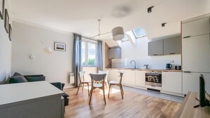 A modern kitchen with white cabinets, a built-in oven, and a dining area with wooden chairs and a white table.