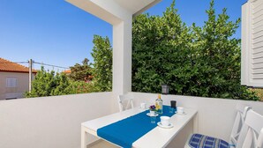 A balcony with a white table and chairs, a blue table runner, and a bottle of liquor. - Amazing apartment in Kosljun with WiFi (Kosljun)