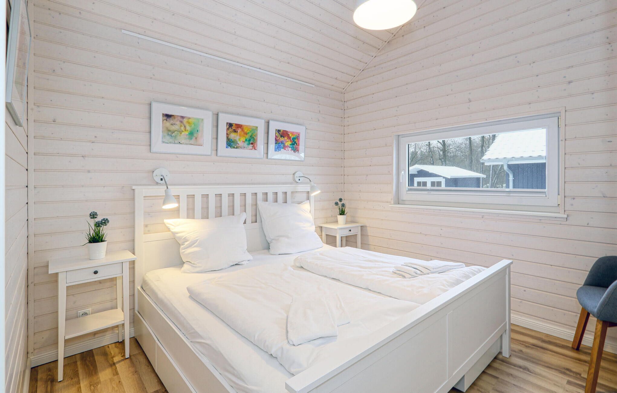 Ein Schlafzimmer mit einem weißen Bett, Nachttischen, einem Fenster und Bildern an der Wand.