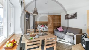 A modern living room with a wooden dining table, chairs, a sofa, and a large window. - attraktive Ferienwohnung (Klösterle)