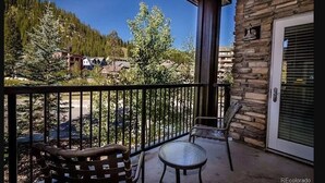 A balcony with a stone wall, a door with a window, and a view of houses and trees. - Location and Comfort - One Bedroom Ski In / Ski out, Hot Tub and Fire Pit (Winter Park)
