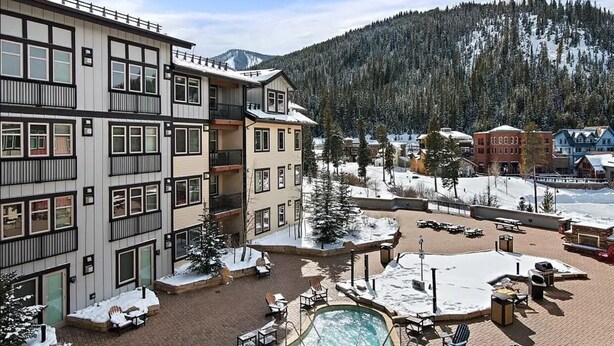 A multi-story hotel with a pool area, outdoor seating, and a view of snow-covered mountains. - Location and Comfort - One Bedroom Ski In / Ski out, Hot Tub and Fire Pit (Winter Park)