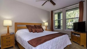 A bedroom with a large bed, two bedside tables, a ceiling fan, a TV, and a window with curtains. - Location and Comfort - One Bedroom Ski In / Ski out, Hot Tub and Fire Pit (Winter Park)