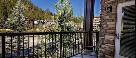 Un balcon avec un mur en pierre, une porte dotée d’une fenêtre et une vue sur des maisons et des arbres.