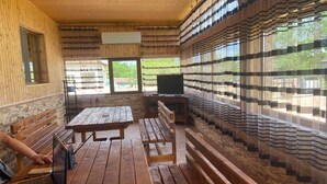 Una cabaña de madera con una mesa grande y bancos, un televisor y una ventana con cortinas.