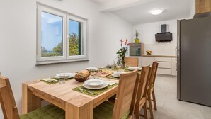 Een eetruimte met een houten tafel voor vier personen, een keuken met moderne apparatuur en een raam met uitzicht op groen.