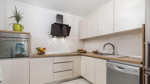 Een moderne keuken met witte kasten, een roestvrijstalen oven, een vaatwasser en een gootsteen met een zwarte kraan.