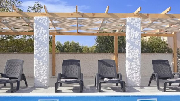 Een zwembadgedeelte met drie ligbedden onder een pergola met witte zuilen.