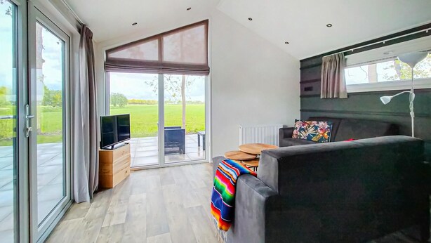 A modern living room with a sofa, a television, and a view of a green landscape through large windows. - Amazing home in Oosterwolde (Oosterwolde)