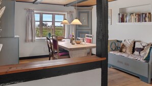 A dining area with a wooden table, chairs, and pendant lights. There is a window with curtains and a view of greenery outside. A bookshelf with books is visible in the background. - 2 bedroom nice home in Harpelunde (Harpelunde)
