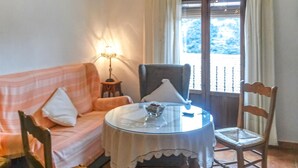 Une pièce confortable avec un canapé, une table et une chaise. Il y a une lampe sur une table d'appoint, et une fenêtre donnant sur des arbres.