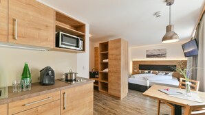Habitación de hotel compacta con kitchenette, una cama con cabecera, una mesa de comedor y un televisor.