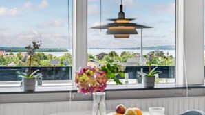 Ein Zimmer mit großem Fenster und Blick auf eine schöne Landschaft, einer hängenden Pendelleuchte und einem Tisch mit Blumenvase.
