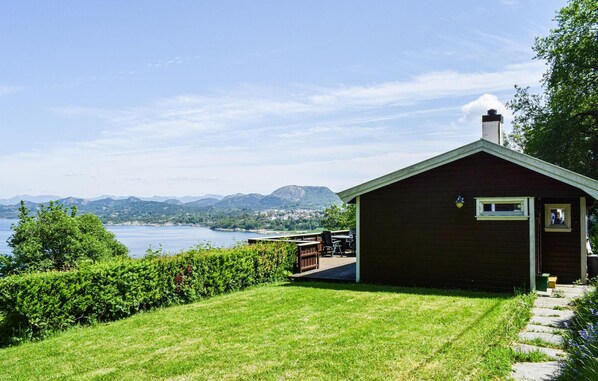 A small wooden cabin with a deck overlooking a lake and mountains.