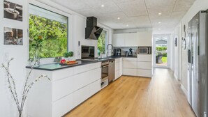 Una cocina moderna con armarios blancos, suelo de madera y vistas a zonas verdes.
