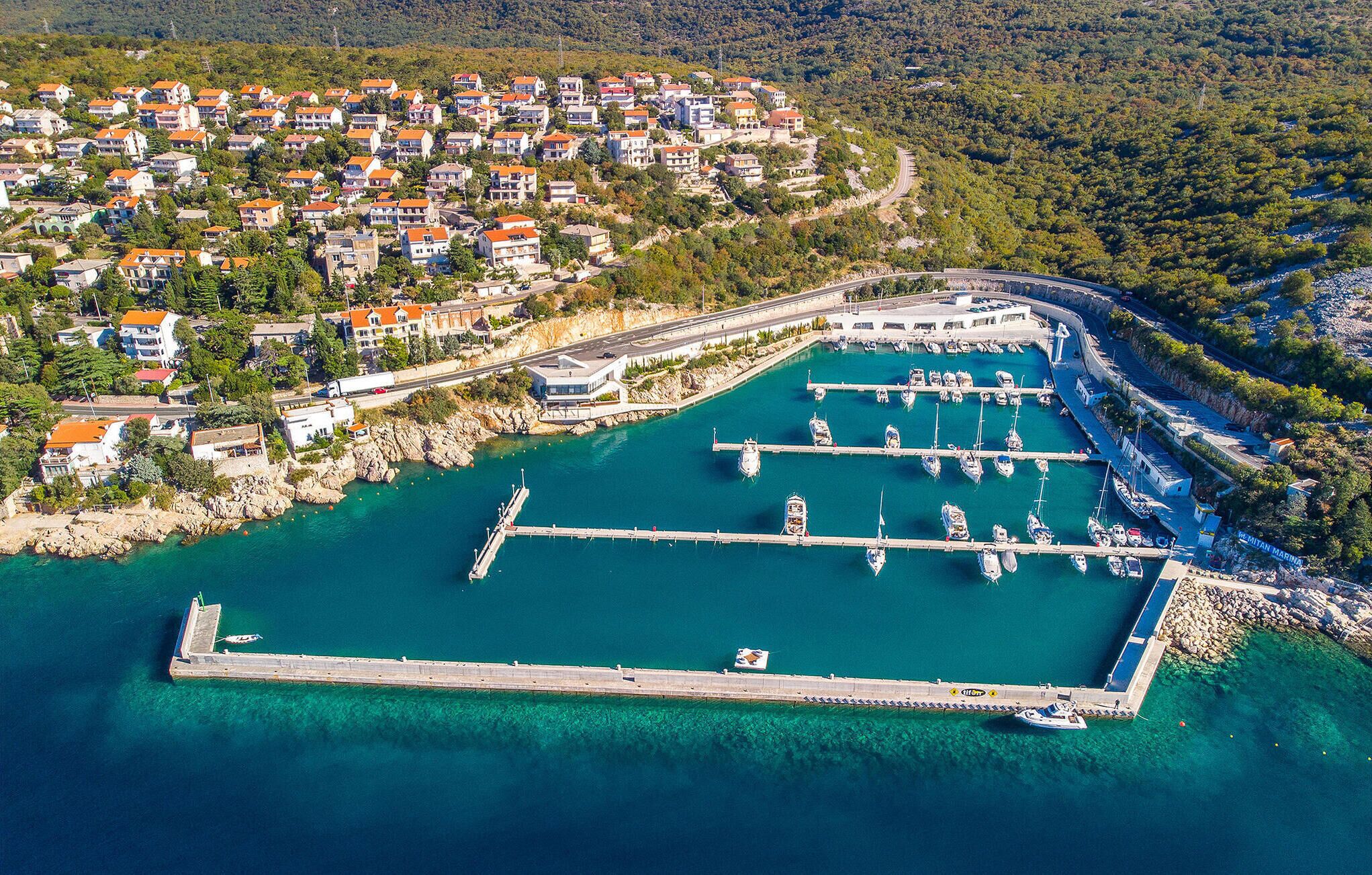 Vue aérienne d’une ville côtière avec un port de plaisance, des immeubles résidentiels et une côte rocheuse.