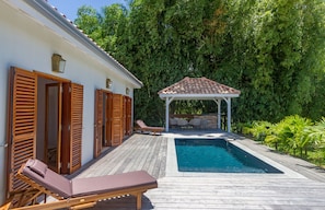 A wooden deck with a swimming pool, lounge chairs, and a gazebo.