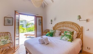 A bedroom with a bed, a chair, a door leading to a balcony, and a wall-mounted lamp.