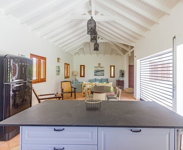 A kitchen with a black countertop, white cabinets, a dining area with a round table, and a ceiling with exposed beams.