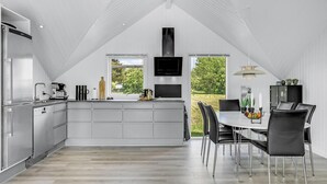 Une cuisine moderne dotée d’un îlot central, d’un coin repas avec une table et des chaises, et d’une grande fenêtre offrant une vue sur la verdure.