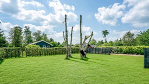 Un espace verdoyant bien entretenu, avec un hamac suspendu entre des arbres, une haie et une maison en arrière-plan.