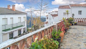 A stone-paved terrace with potted plants, white buildings with red-tiled roofs, and a clear sky. - Amazing apartment in Genalguacil (Genalguacil)