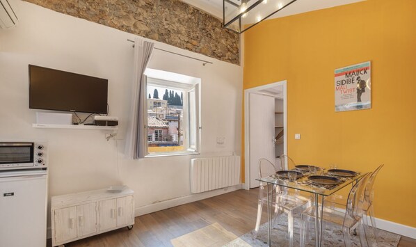 A modern kitchen with a built-in oven, microwave, and refrigerator. There's a dining area with a glass table and chairs, and a large window offering a view of the city. - Old Nice- Jean Jaurès FSHH (NICE)