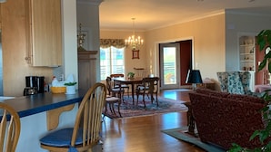A spacious living area with a wooden dining table, chairs, and a sofa. A kitchen area with a counter and cabinets is visible to the left. - Quiet, Spacious House Close to SML and Liberty University (Moneta)