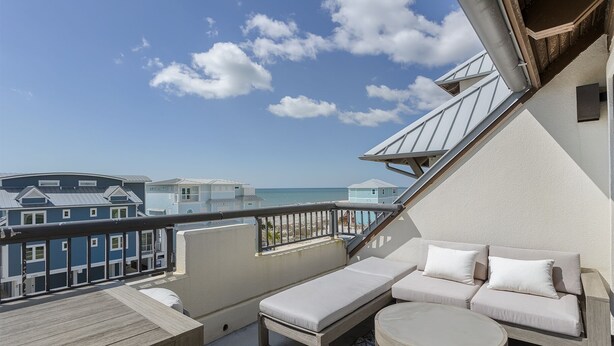 A balcony with a sofa and a small table, overlooking a beach with buildings in the background. - Beach Paradise - Perfect Ocean Sunset Views with Pool & Sauna & Breakfast! (Mexico Beach)