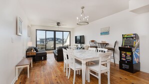 A dining area with a white table and chairs, a ceiling fan, a TV, and a gaming console. - Beach Paradise - Perfect Ocean Sunset Views with Pool & Sauna & Breakfast! (Mexico Beach)
