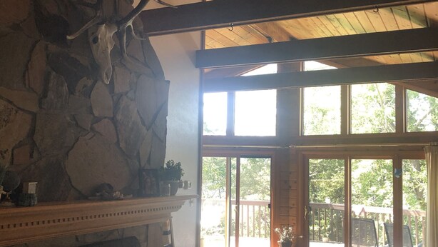 Ein rustikales Interieur mit Kamin aus Stein, Holzbalken und einer großen Schiebeglastür, die auf eine Außenterrasse führt.