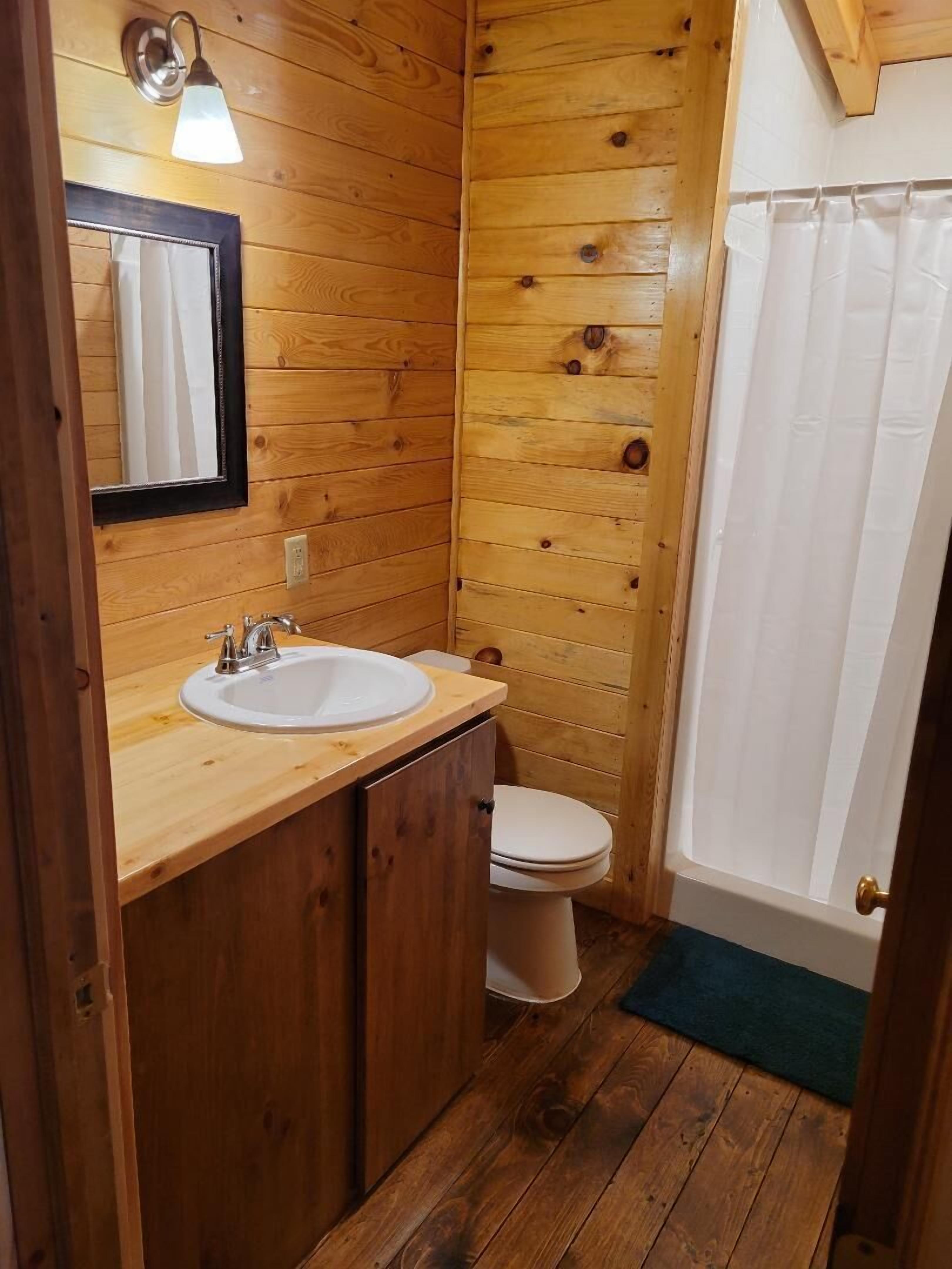 Ein Badezimmer einer Holzhütte mit einem Holzbacheng, einer Toilette und einer Duschvorhang.