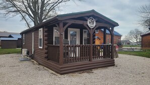 Een klein houten huisje met een veranda, een bordje dat aangeeft dat het een wandelhut is, en een grindpad.