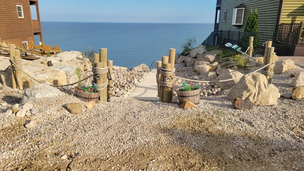 Een kustgebied met een houten terras, een touwbordeshek en uitzicht op de zee.