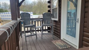Een houten terras met twee Adirondack-stoelen en een kleine tafel.