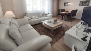 A modern living room with a sofa, coffee table, TV, and dining area. - Allod Park Haus C 207 by Interhome (Davos)