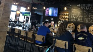 Eine Bar mit Holzhockern, einem Wandfernseher und einer Kreidetafel-Speisekarte.