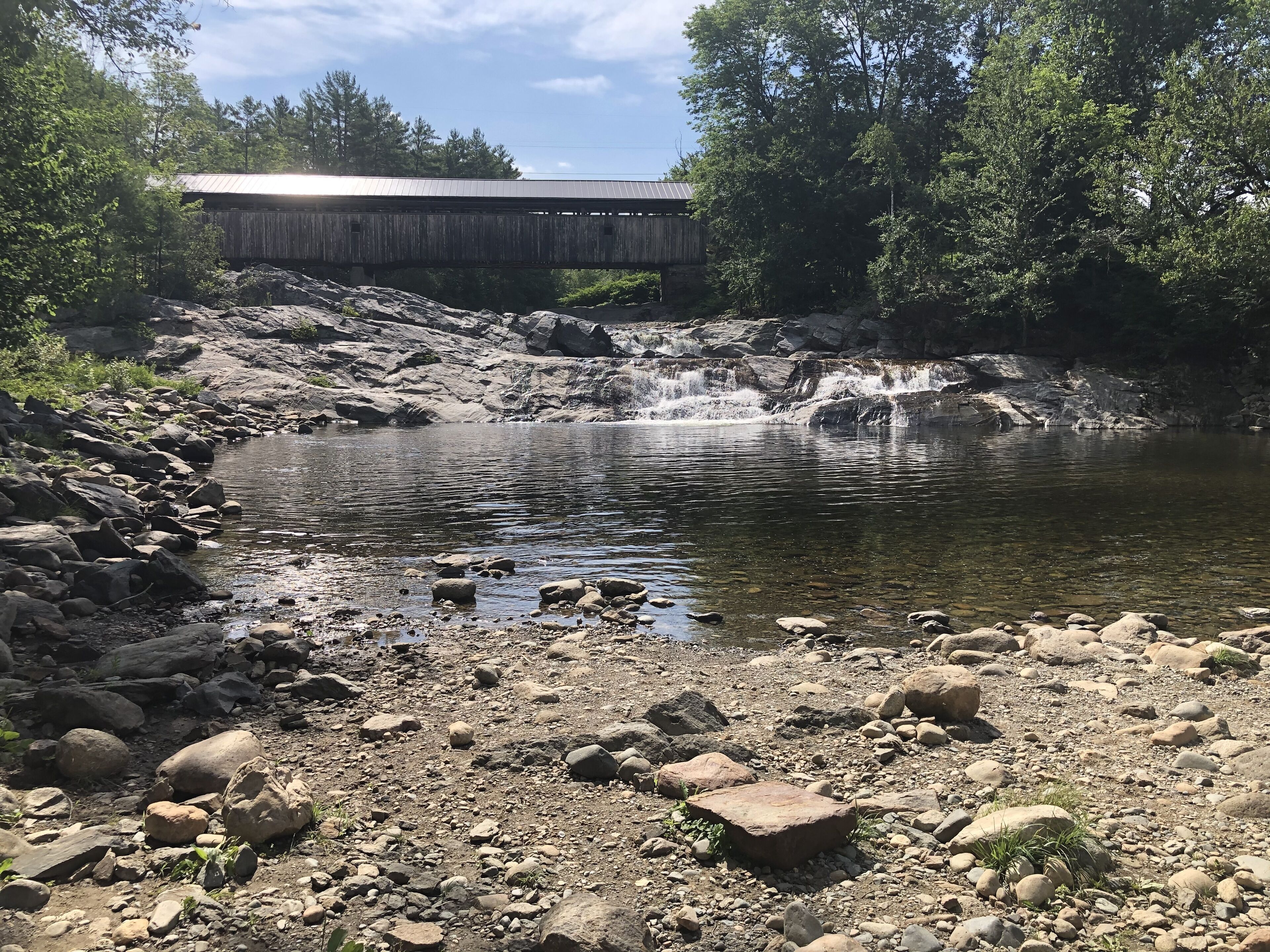 Ein felsiger Flussufer mit einer Holzhütte im Hintergrund.