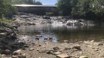 Ein felsiger Flussufer mit einer Holzhütte im Hintergrund.