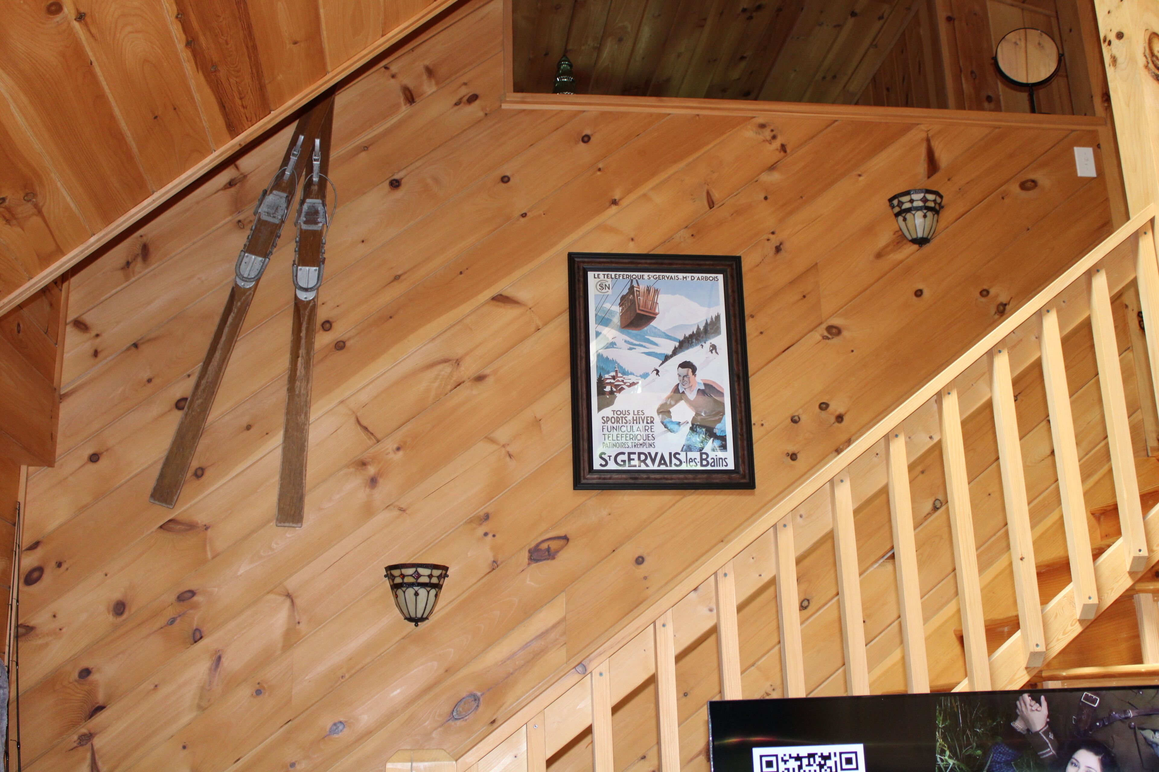 Eine Holzbalkendecke mit Skiausrüstung, einem gerahmten Plakat und einer Treppe.