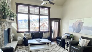 A living room with a fireplace, a large window with a view, a ceiling fan, and a mounted artwork of a bison. - 0.5 mile walk to Gondola and Keystone Village!  50 yards to Keystone Shuttle!   (Keystone)
