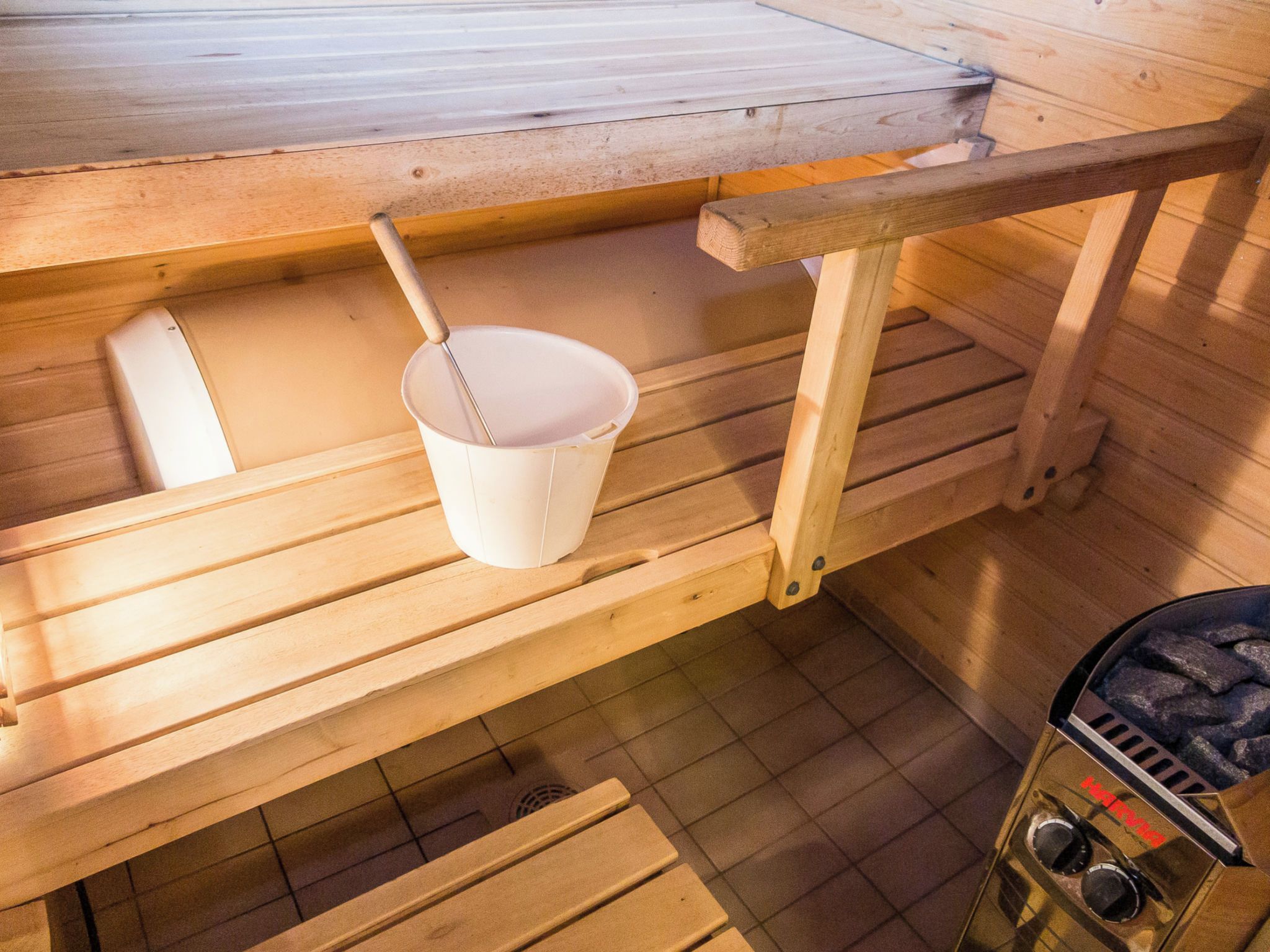 A sauna with wooden benches, a white bucket, and a sauna heater.