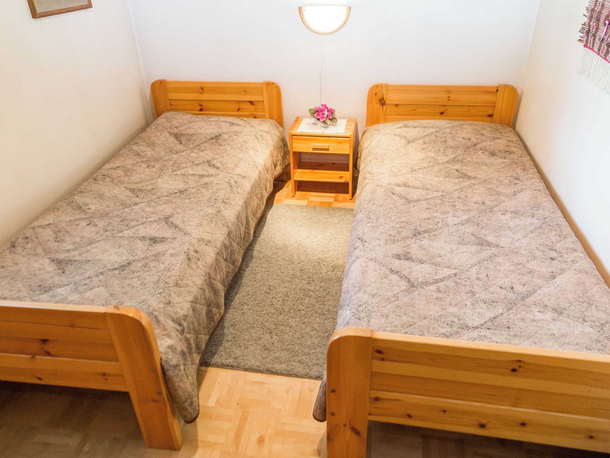 A small room with two wooden beds, a nightstand with a lamp, and a small rug.