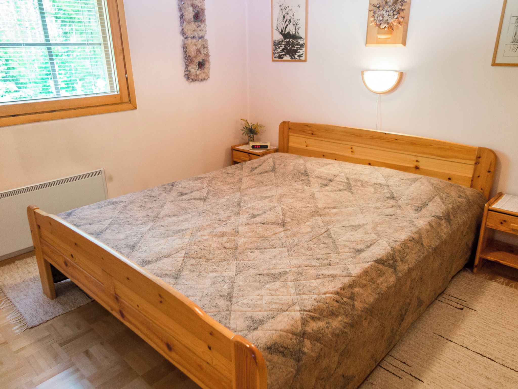 Ein Schlafzimmer mit einem hölzernen Bett, einem Nachttisch mit einer Uhr und einem Fenster mit Jalousien.