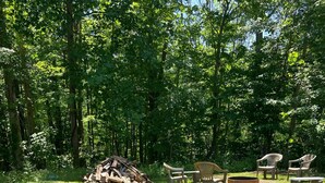 Un espacio al aire libre con césped, una pila de leña, una mesa de picnic y varias sillas de plástico.